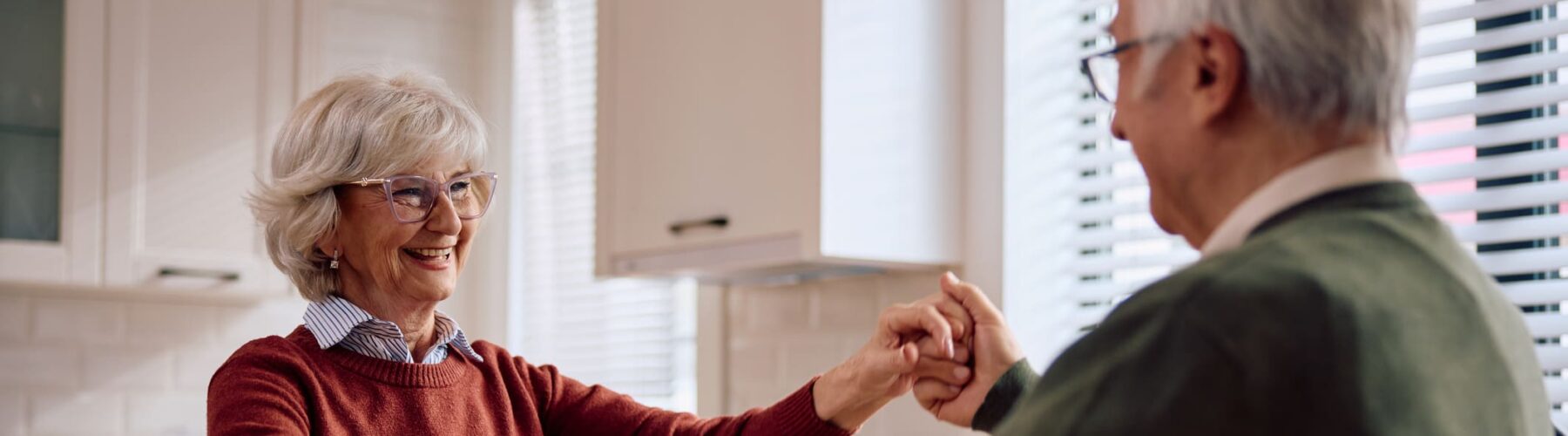 Happy elderly couple dancing at home - Grace Management Seniors joyfully dance together in a modern kitchen, radiating warmth and connection in a vibrant atmosphere.