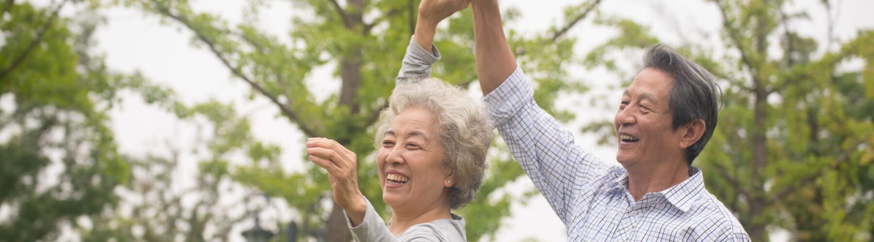 Joyful elderly couple dancing outdoors, surrounded by lush greenery, embodying a vibrant and playful lifestyle.