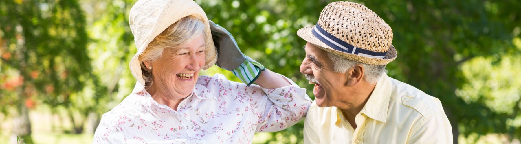 Happy senior couple gardening - Grace Management Joyful seniors gardening together, sharing laughter while holding potted flowers in a vibrant, lush outdoor setting.