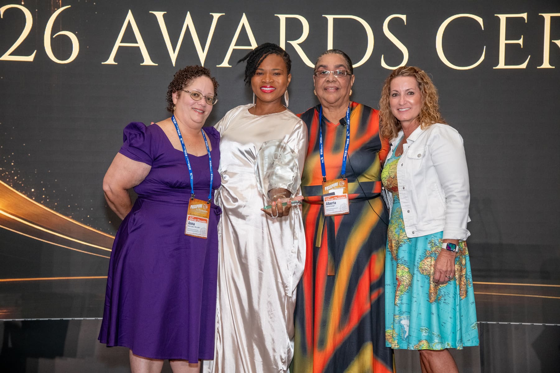 Four women smiling and posing together, holding an award at a ceremony backdrop celebrating achievements.