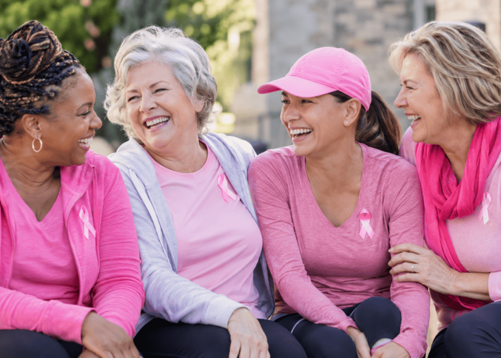 Four women in pink attire share joyful laughter outdoors, celebrating friendship and support, embodying a vibrant lifestyle.