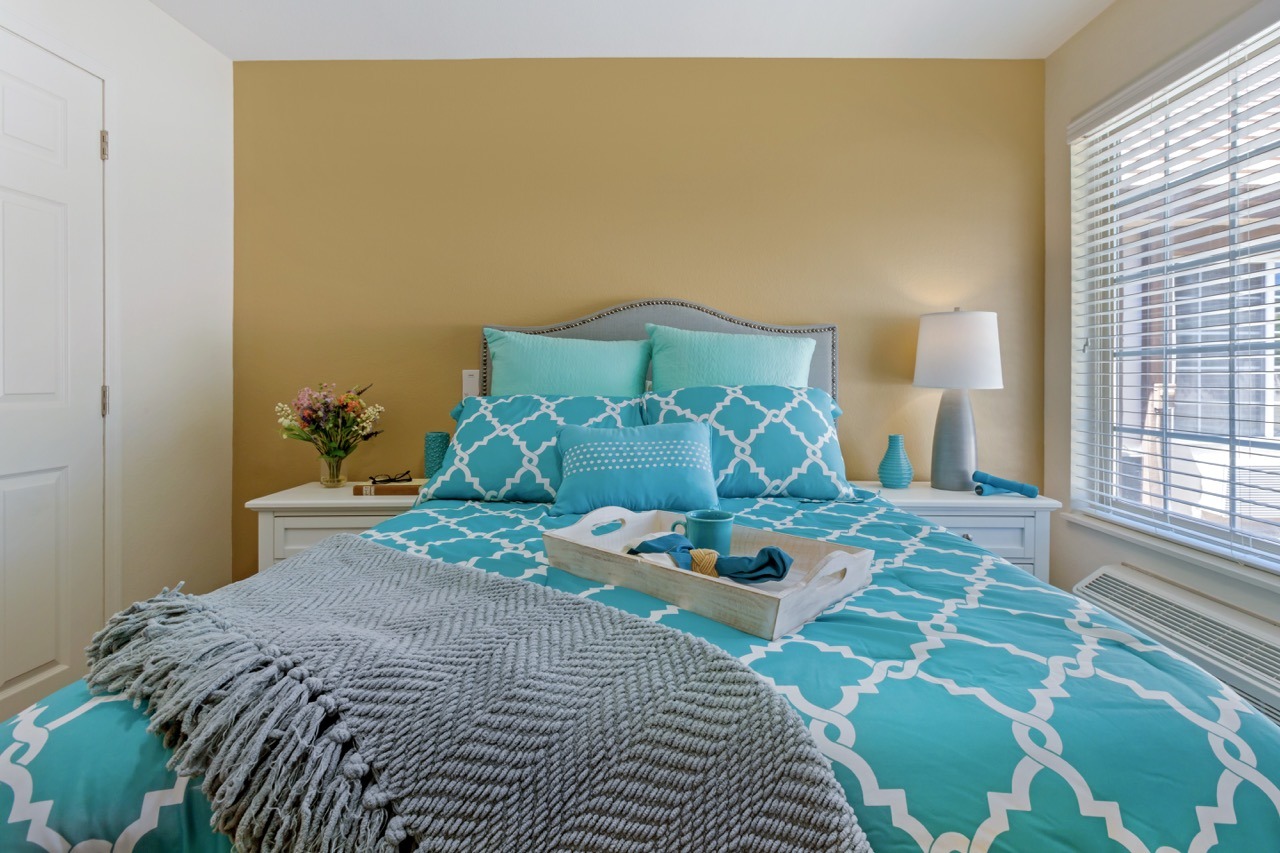 inspirations-of-peoria-sun-city-303A2207-Large - Grace Management Resident's bedroom with warm colored walls and comfortable looking furniture, with lots of natural light. Inspirations of Peoria senior living.