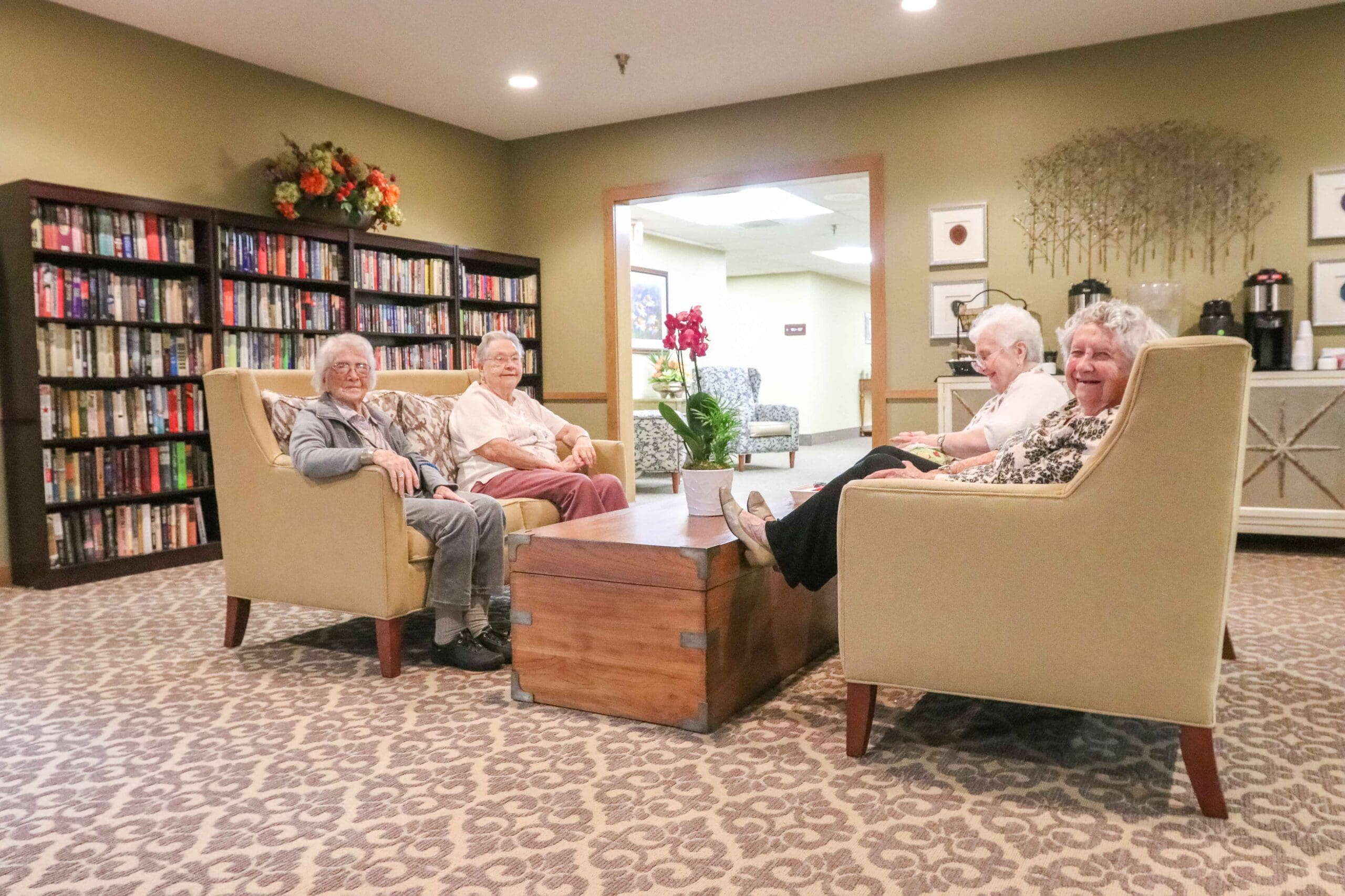 IMG_9796-scaled - Grace Management Residents sit in the common area, enjoying comfortable chairs, a library, and free coffee services at Inspirations at Bartlesville.