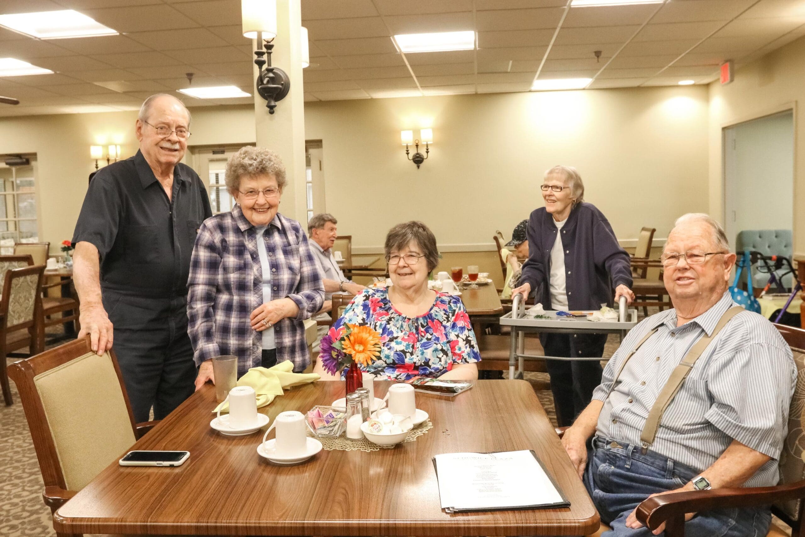 IMG_9751-scaled - Grace Management Residents standing around a dining table together in the dining room at Inspirations of Bartlesville.